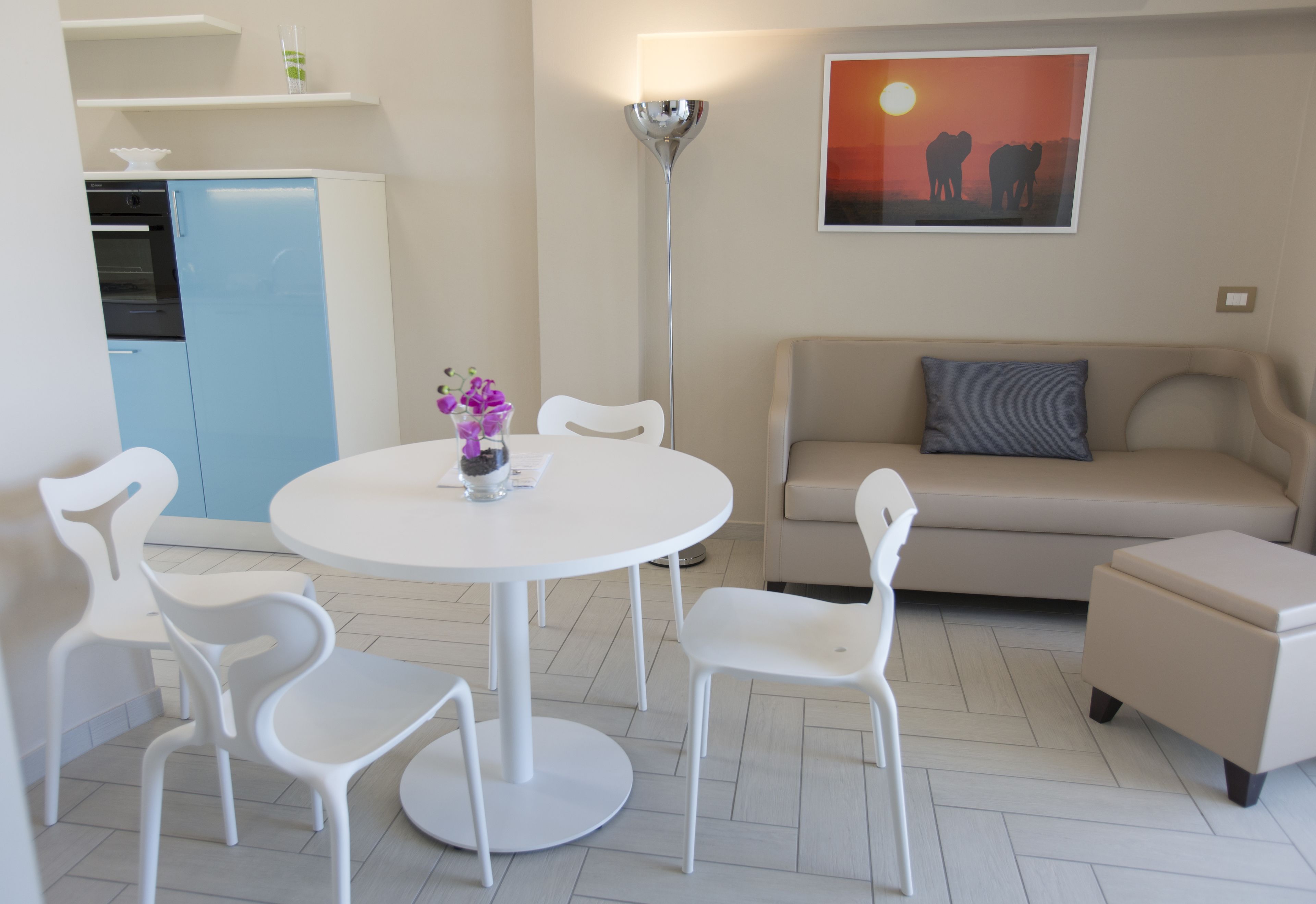 Un salon moderne avec une table ronde blanche, des chaises blanches, un canapé beige et un lampadaire.