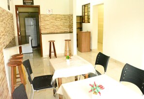 A dining area with a table, chairs, stools, and a refrigerator in the background. - Lize Hotel-Hostel (Campinas)
