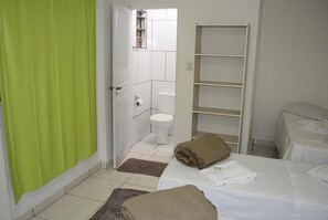 A hotel room with a bed, a bathroom with a toilet and shower, and a shelf unit.