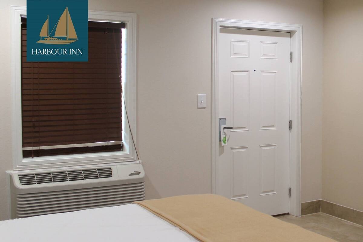 A hotel room with a window, a door, and a bed.