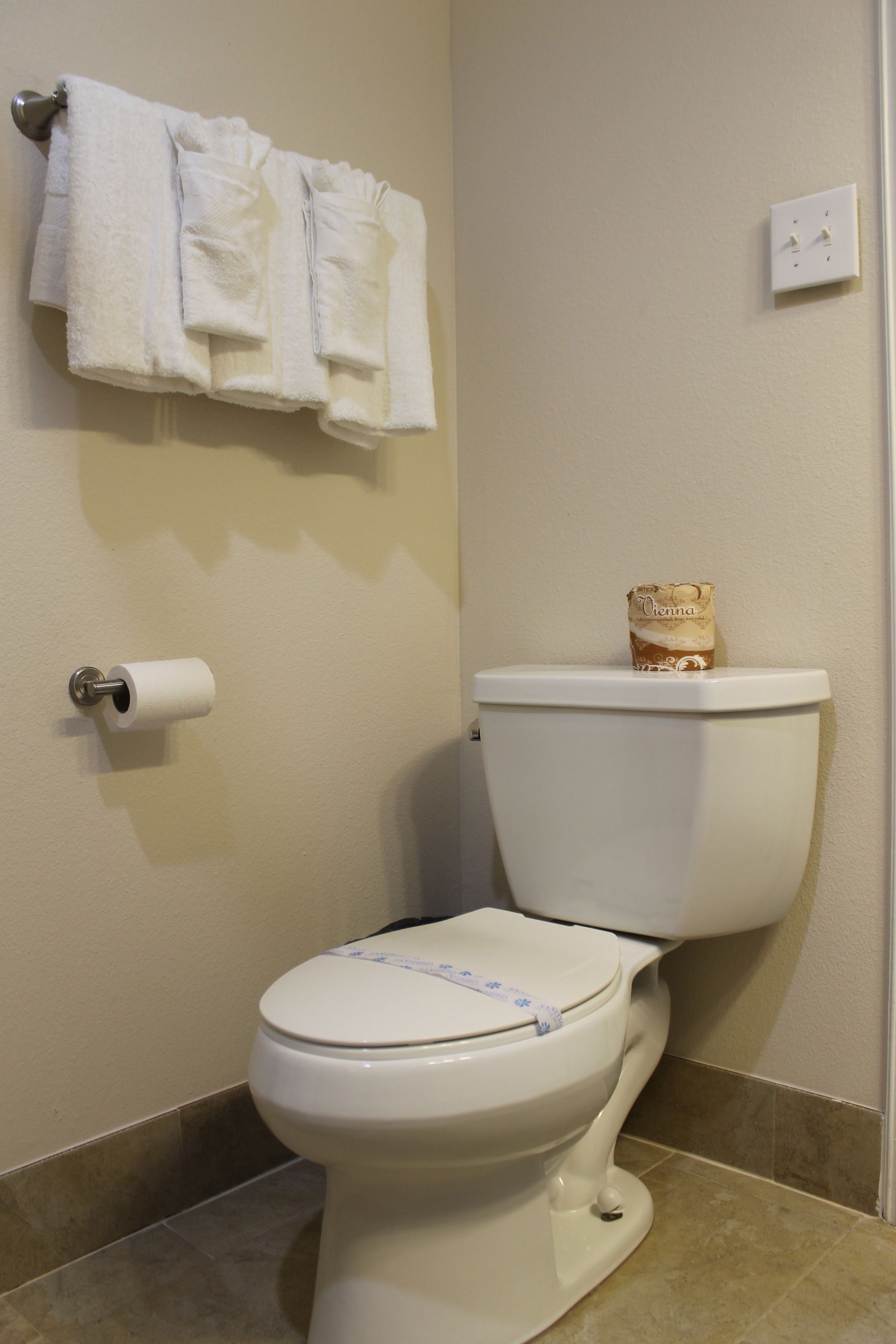 A bathroom with a toilet, a roll of toilet paper, and a package of toilet paper on the toilet lid.