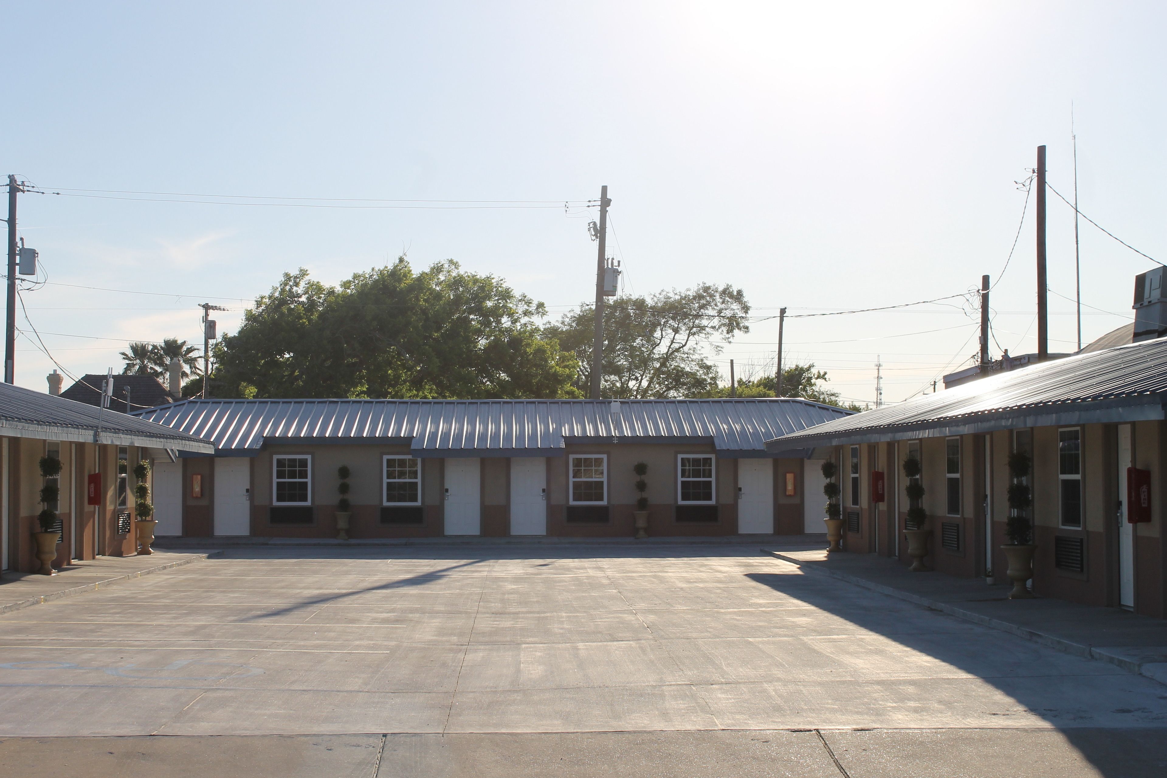 A row of single-story buildings with a central open area, likely a parking lot, and a clear sky.