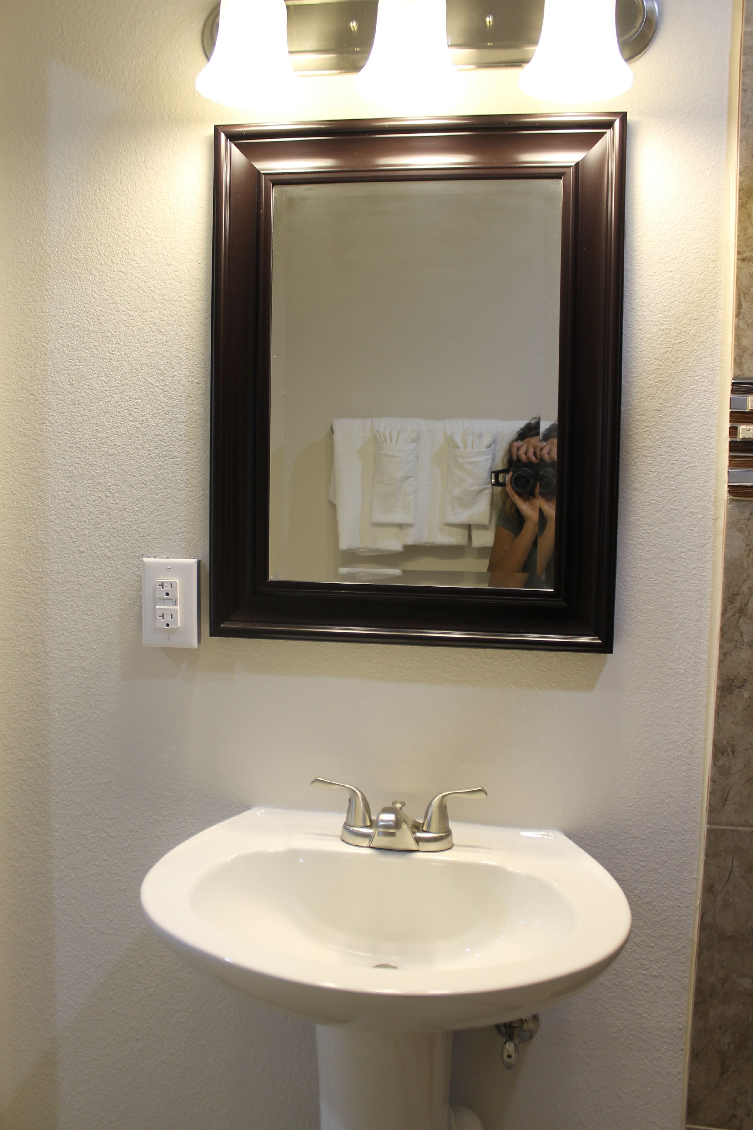 A bathroom with a white sink, a dark-framed mirror, and a light fixture above the mirror.