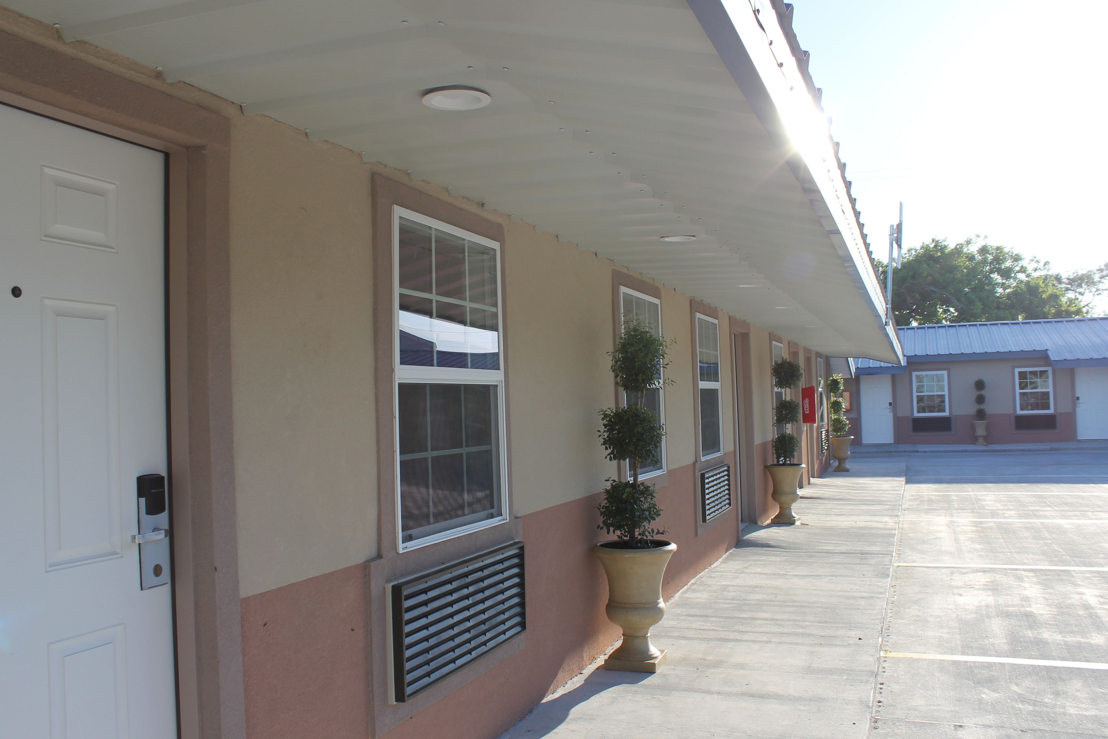 A hotel exterior with a row of windows, a covered walkway, and potted plants.