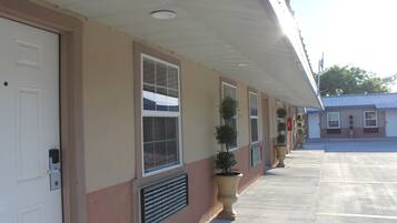 A hotel exterior with a row of windows, a covered walkway, and potted plants.
