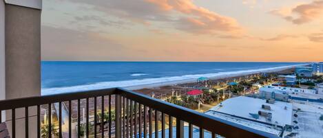 A balcony with a view of the beach and ocean during sunset.