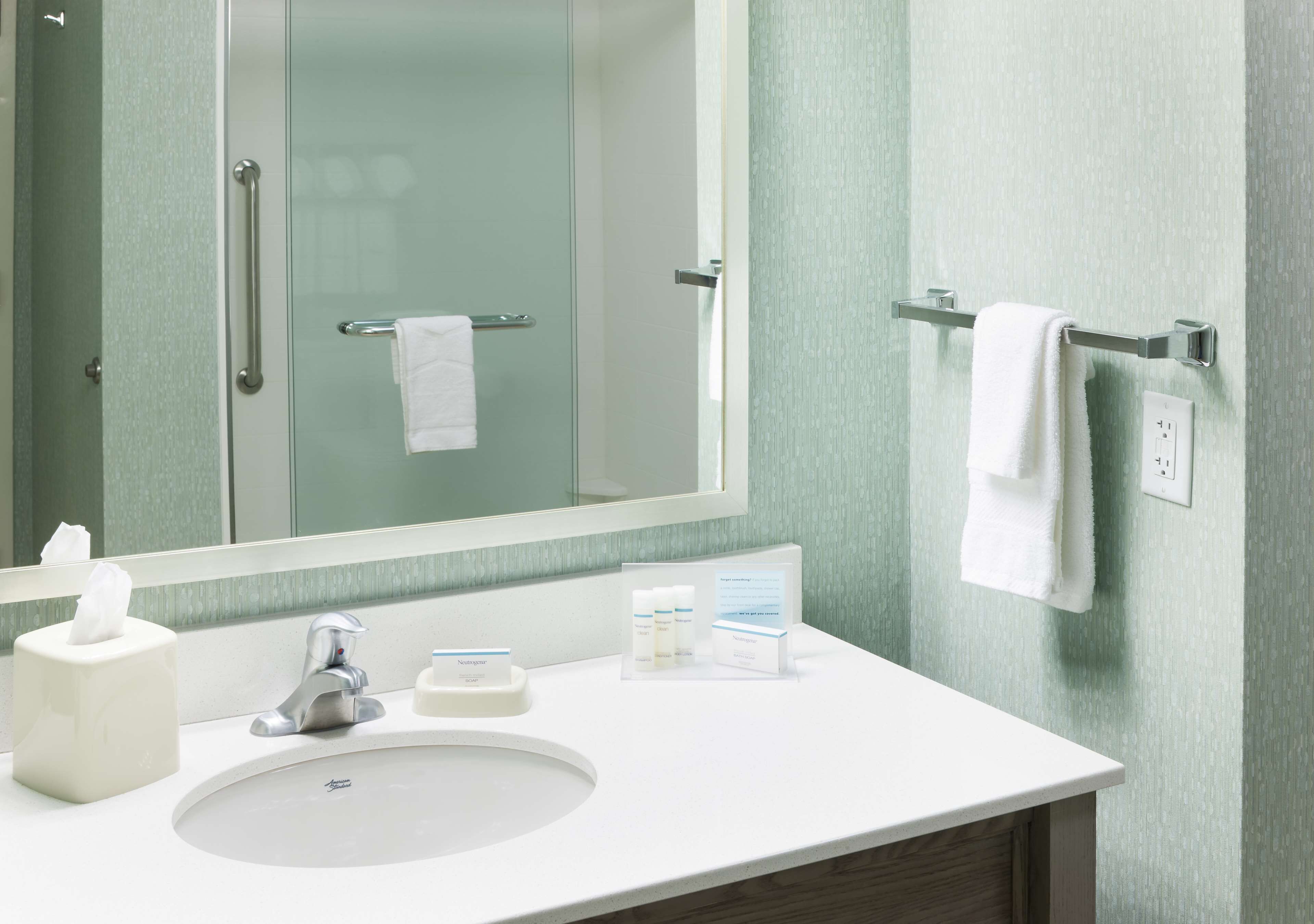 A bathroom with a white sink, a mirror, a towel rack, and a hand sanitizer dispenser.