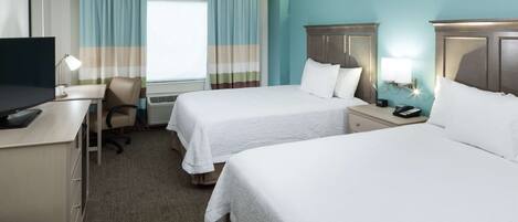 A hotel room with two beds, a desk with a TV, a chair, and a desk lamp.