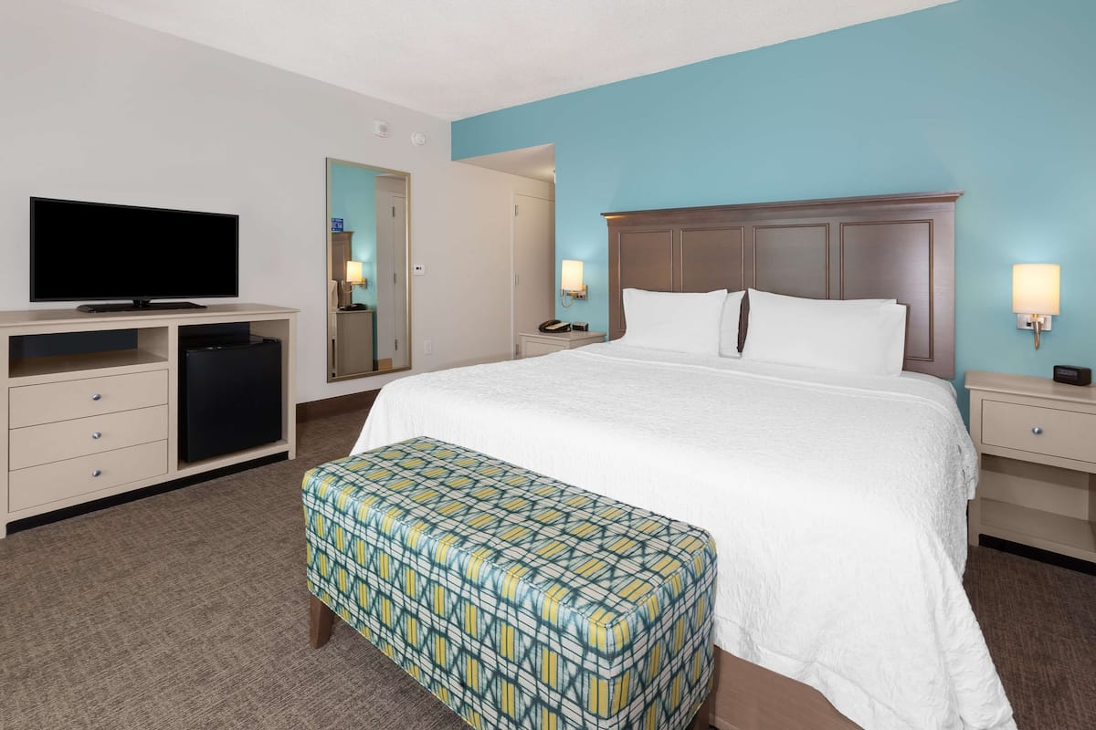A hotel room with a large bed, a television, a desk, and a bench.