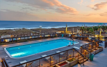 A pool area with a wooden deck, lounge chairs, and a view of the ocean.