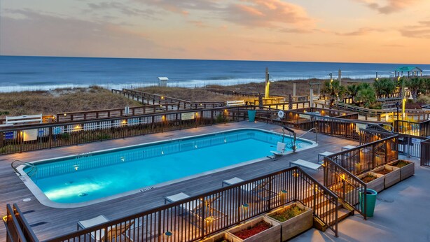 A pool area with a wooden deck, lounge chairs, and a view of the ocean. - Hampton Inn & Suites Carolina Beach Oceanfront (Carolina Beach)