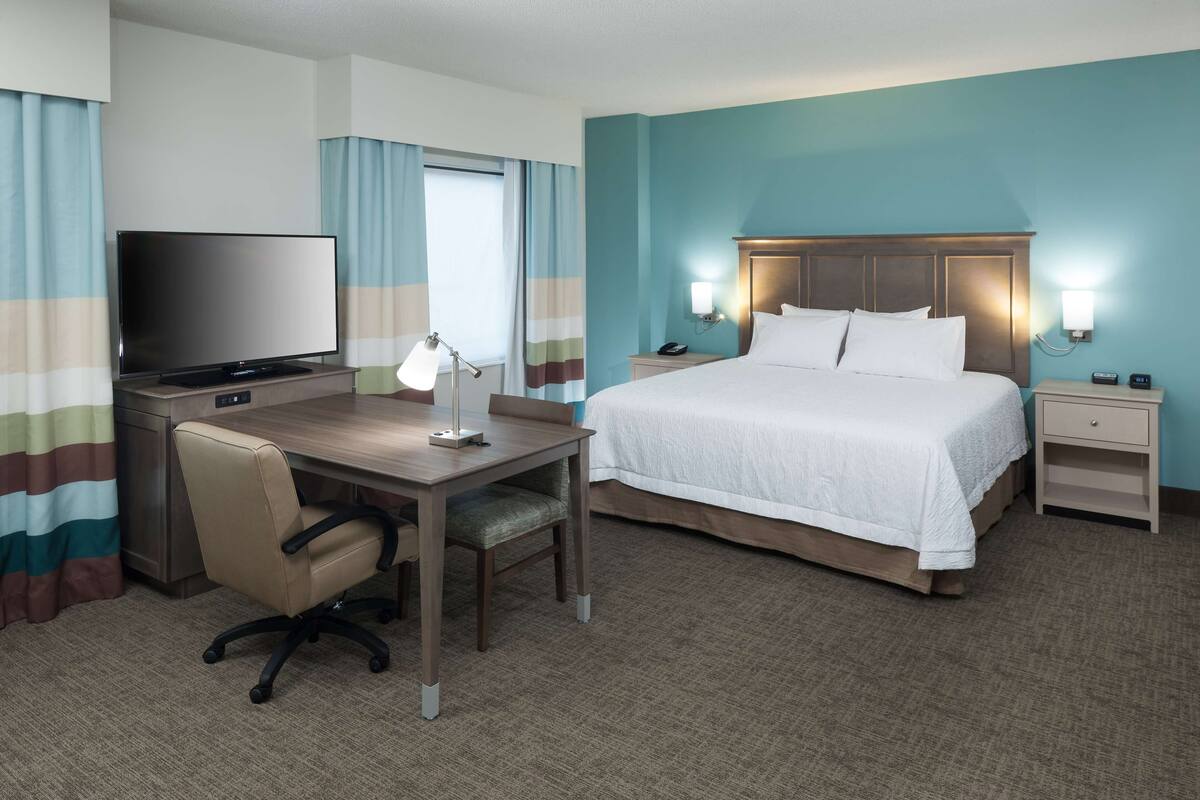 A hotel room with a bed, desk, chair, TV, and bedside lamps.