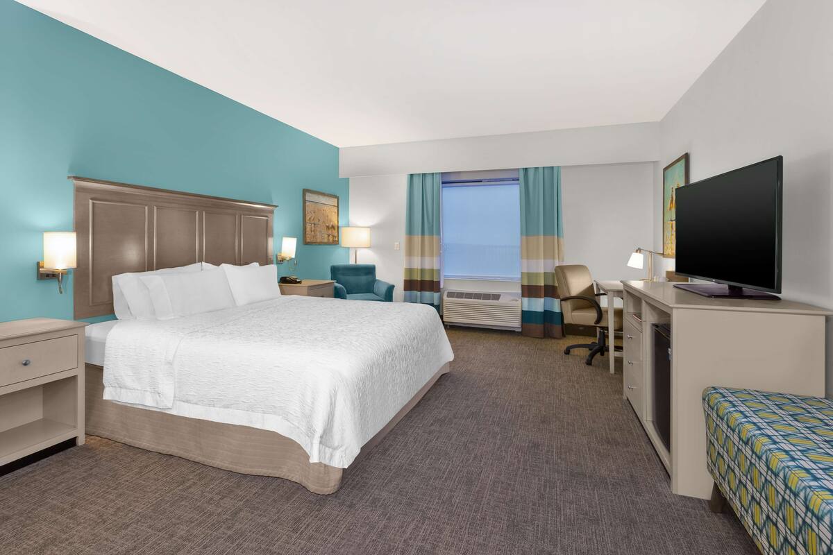 A hotel room with a bed, desk, chair, TV, and a window with curtains.