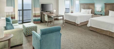 A hotel room with two beds, a desk with a TV, a sofa, and a balcony with curtains.