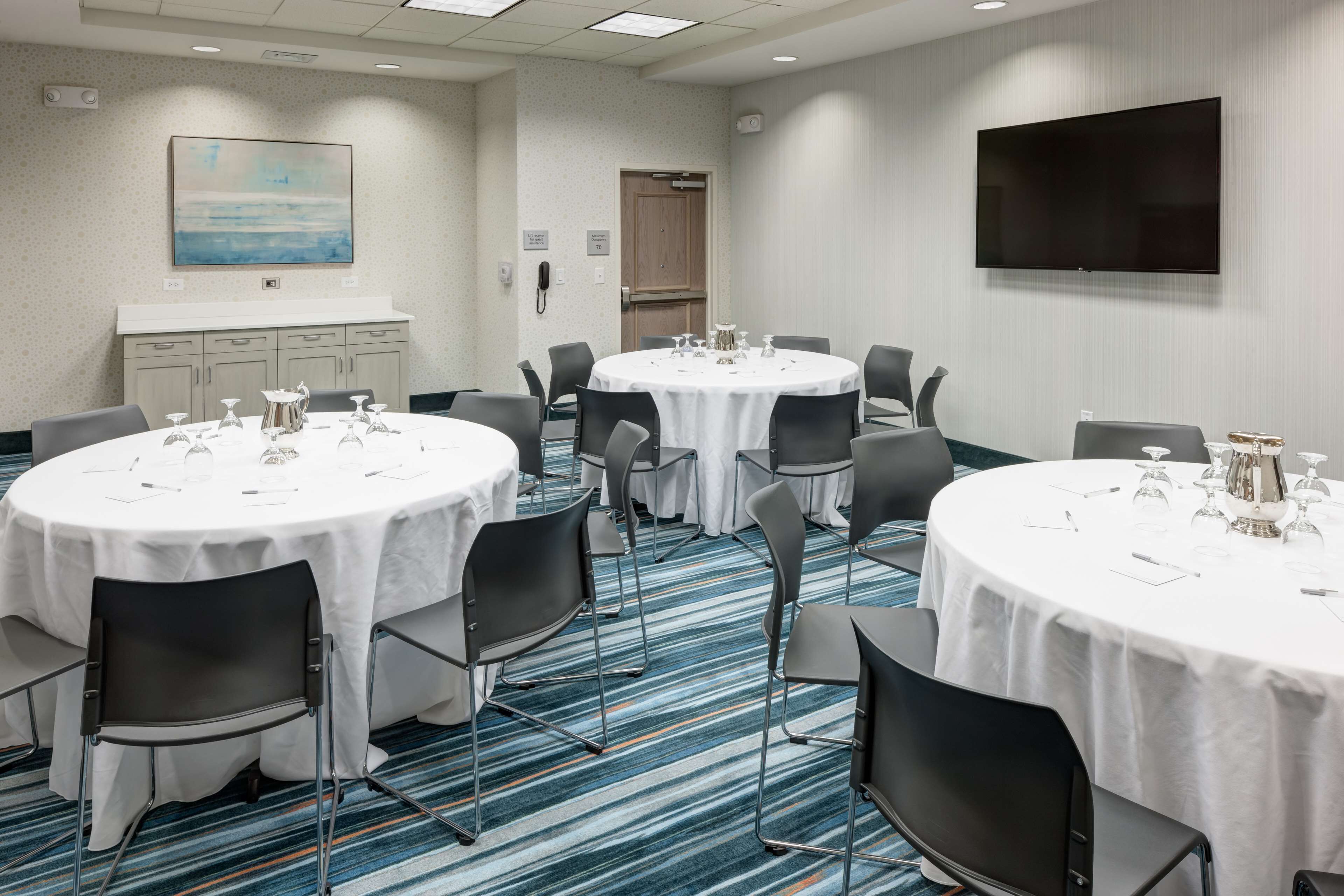 A conference room with round tables, chairs, and a flat-screen TV.