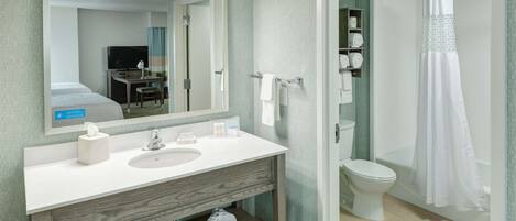A bathroom with a white sink, mirror, and toilet. There is a shower curtain and a towel rack visible.