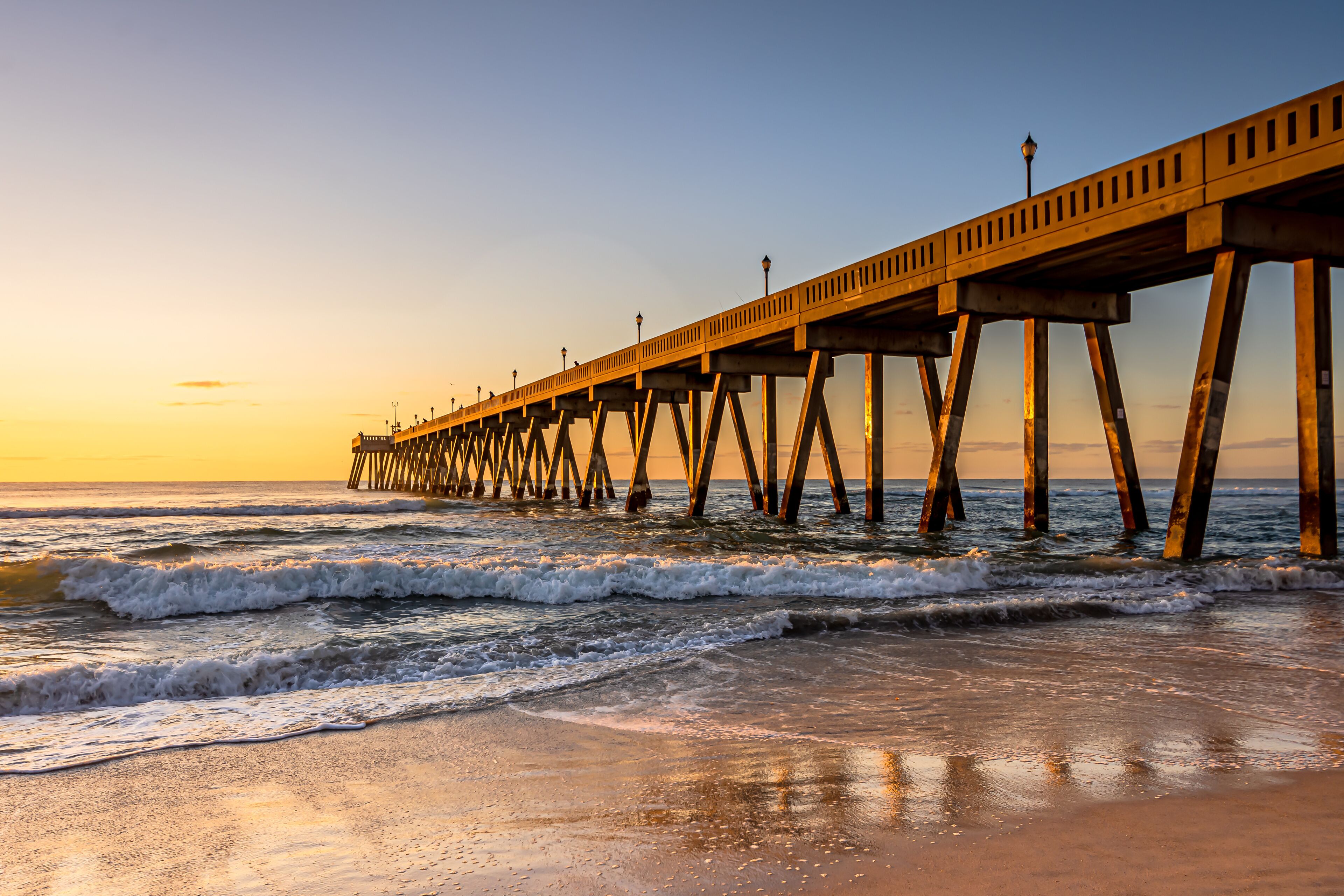 Un muelle se adentra en el océano con un atardecer de fondo.