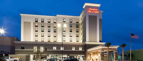 A Hampton Inn & Suites hotel with a parking lot, multiple cars, and an American flag.