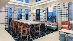 A spacious hotel lobby with a long dining table, multiple seating options, and large windows offering views of the outside. - Hampton Inn & Suites Carolina Beach Oceanfront (Carolina Beach)