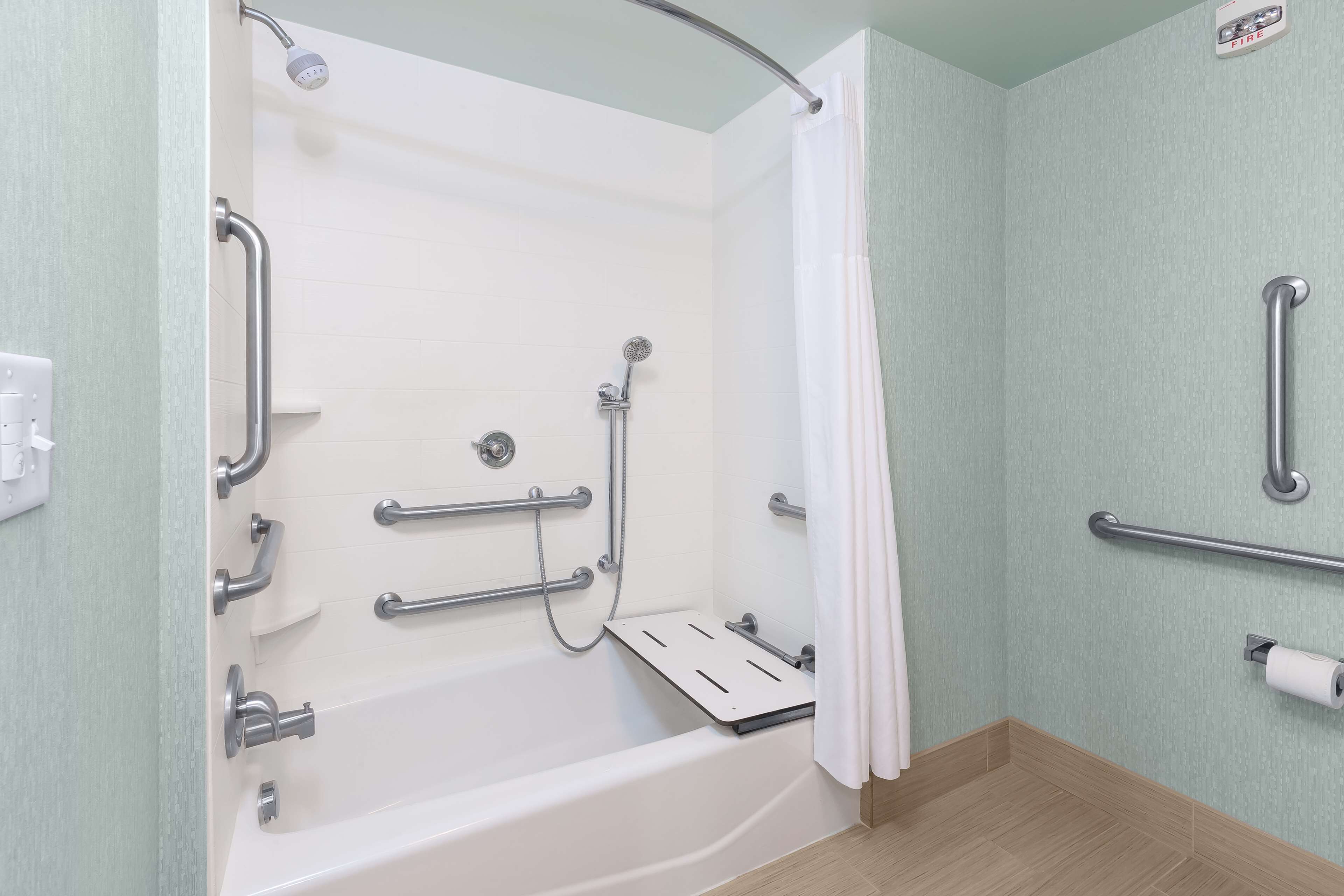 Un baño con una bañera blanca, barras de apoyo, un cabezal de ducha y un dispensador de papel higiénico.