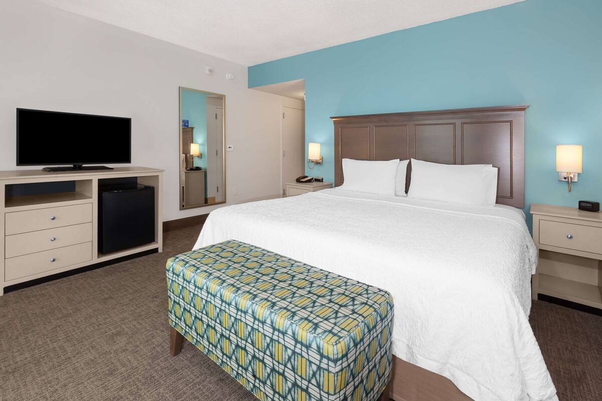 A hotel room with a bed, a television, a desk, a mirror, and a nightstand.