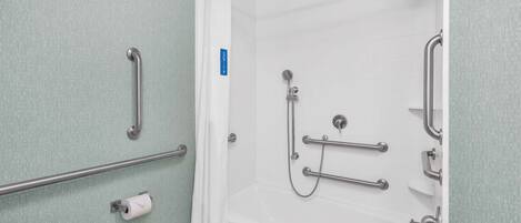 A bathroom with a shower, grab bars, and a toilet paper holder.