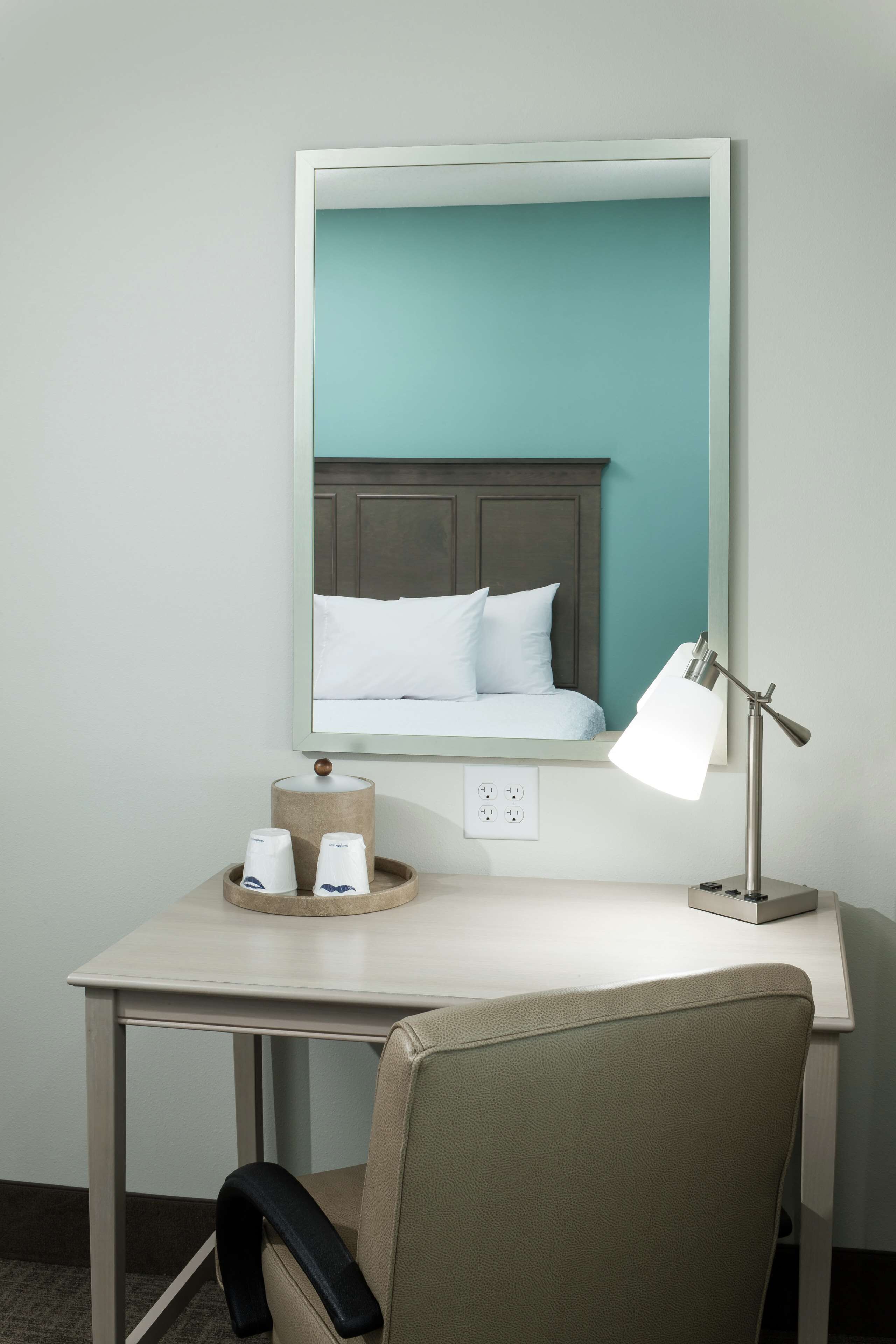 A hotel room with a bed, a desk, a chair, a lamp, and a mirror.