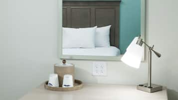 A hotel room with a bed, a desk, a chair, a lamp, and a mirror.