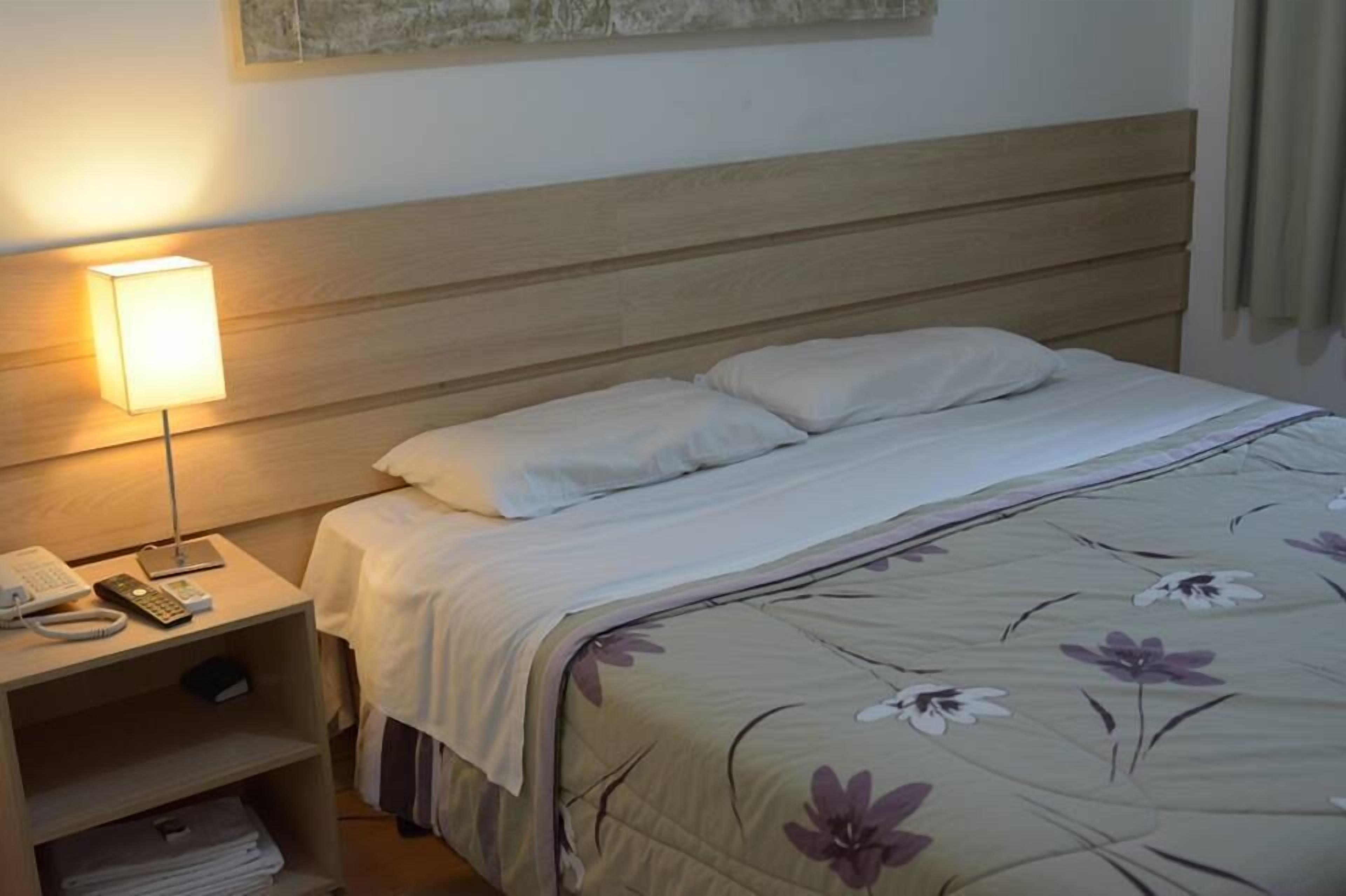 A neatly made bed with a floral bedspread, a bedside lamp, and a nightstand with a phone and remote control.