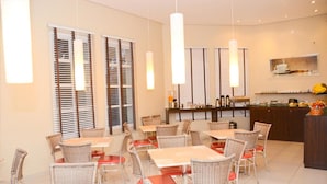 Un espace repas avec des tables et des chaises, un comptoir avec un présentoir, et une fenêtre avec des stores.