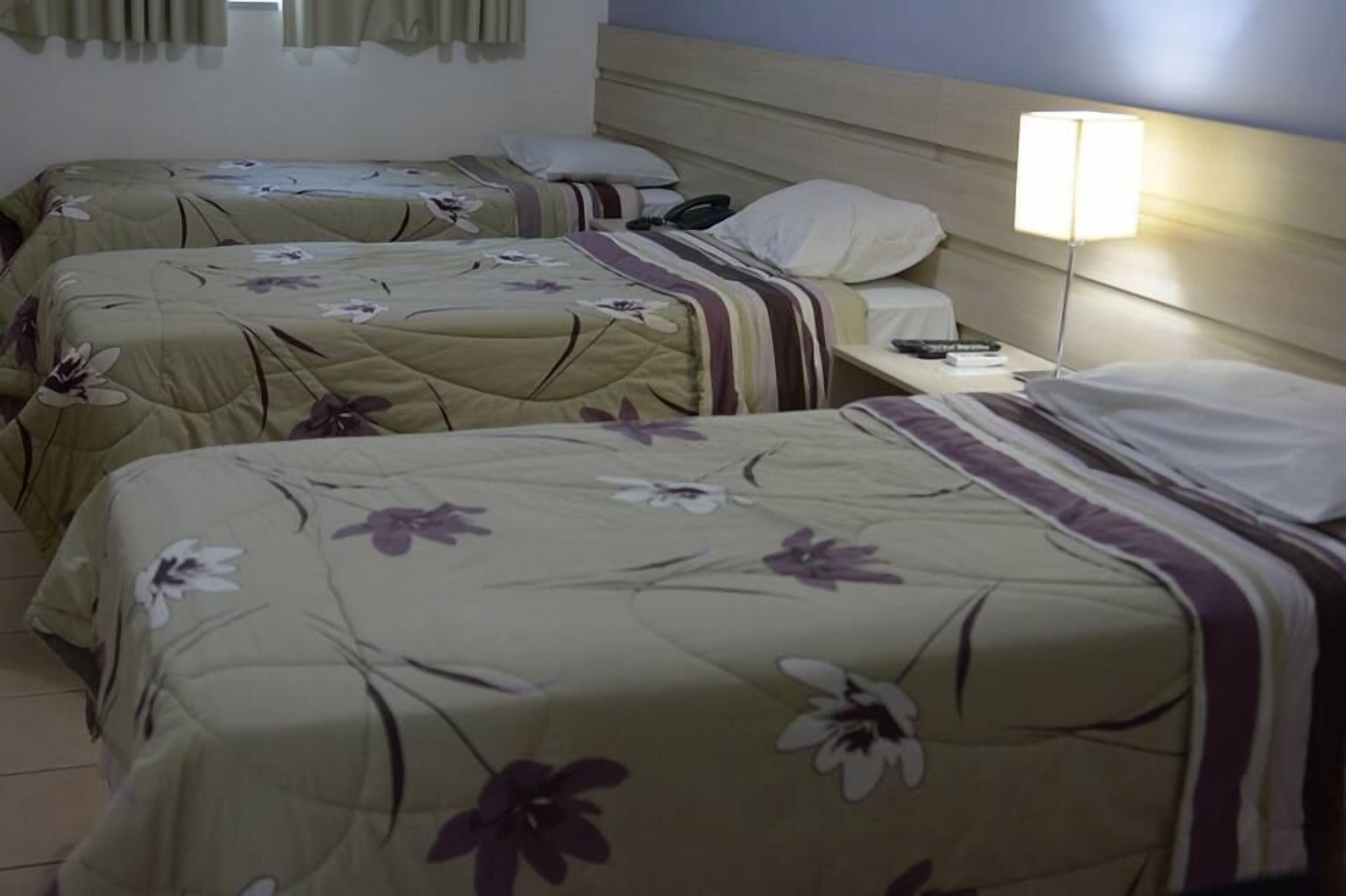 Une chambre d’hôtel avec deux lits, chacun agrémenté d’une literie à motifs floraux et d’une table de chevet avec une lampe.