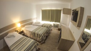 Une chambre d’hôtel avec trois lits, une table de chevet avec une lampe, un miroir et une fenêtre avec des rideaux.