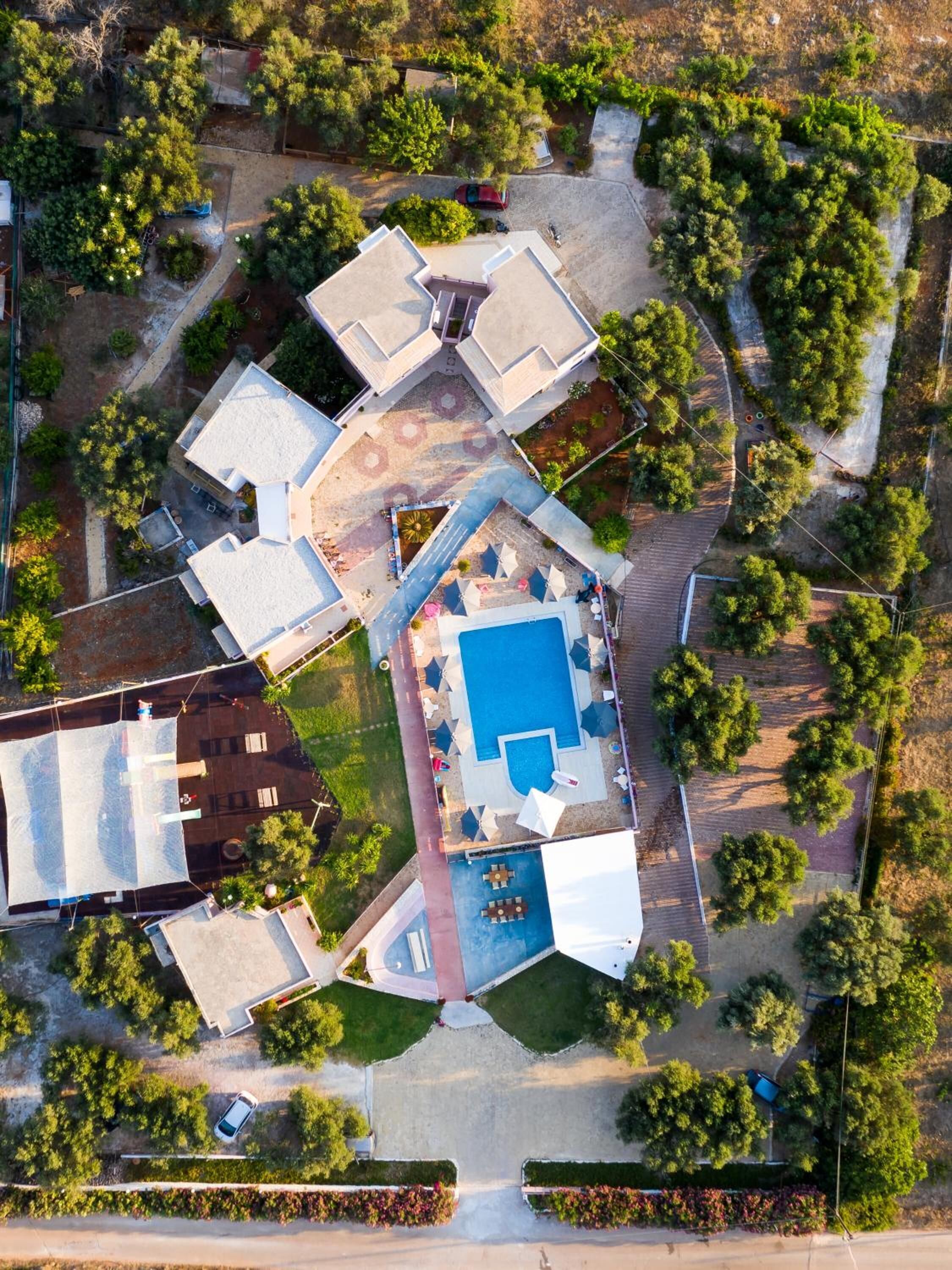 An aerial view of a residential area with multiple houses, a swimming pool, and surrounding greenery.