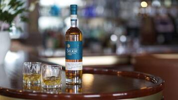 A bottle of whisky and two shot glasses on a round wooden table.