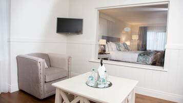 Habitación de hotel con cama, televisor montado en la pared, una silla y una mesa con botellas de agua.