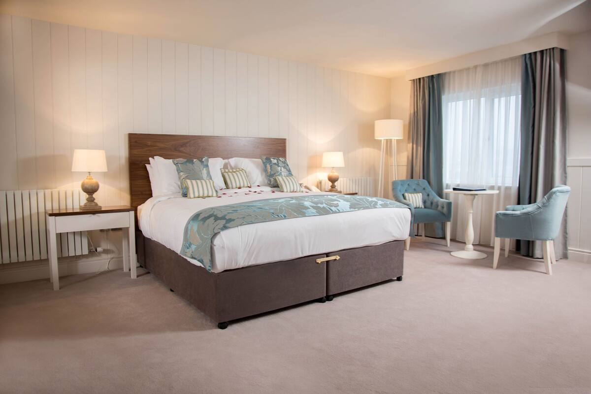 A bedroom with a large bed, two bedside tables, a chair, and a small table.
