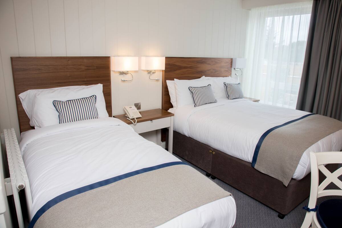 A hotel room with two beds, a wooden headboard, bedside lamps, a telephone, and a window with curtains.