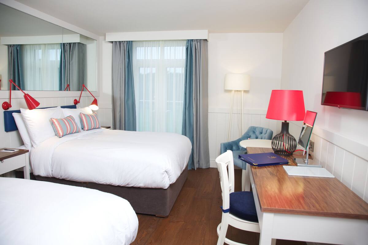 A hotel room with a bed, a desk, a chair, a TV, and a lamp.