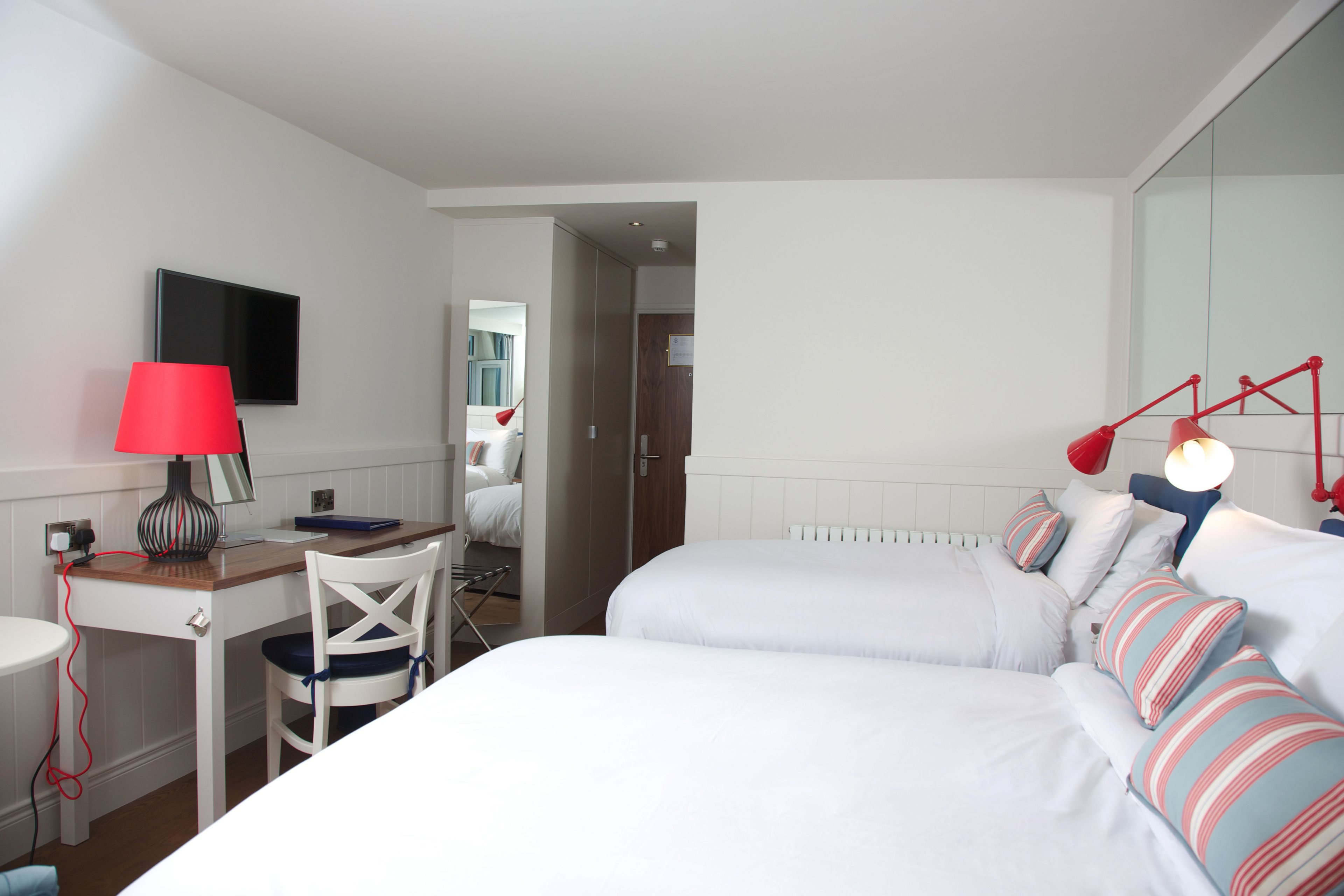 A hotel room with a bed, a desk, a chair, a TV, and a red lamp.