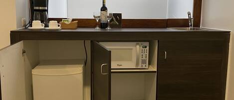 A kitchenette with a microwave, coffee maker, and wine bottle.