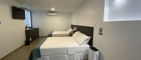 A hotel room with two beds, a TV, a trash bin, and a ceiling light.