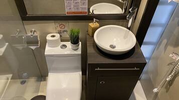 A modern bathroom with a toilet, sink, and shower. There is a sign with handwashing instructions and a small plant on the sink.
