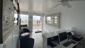 Eine Hotelhalle mit einer Rezeption, einem großen Spiegel, einem Deckenventilator und Blick ins Freie.