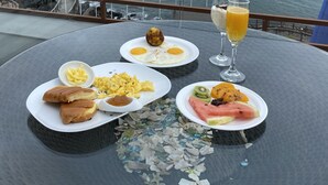 Ein Tisch mit Frühstückstellern, einem Glas Orangensaft und Blick auf das Meer mit Booten.
