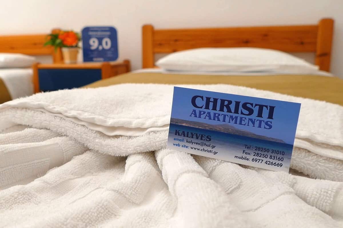 A neatly made bed with a Christi Apartments brochure on it.