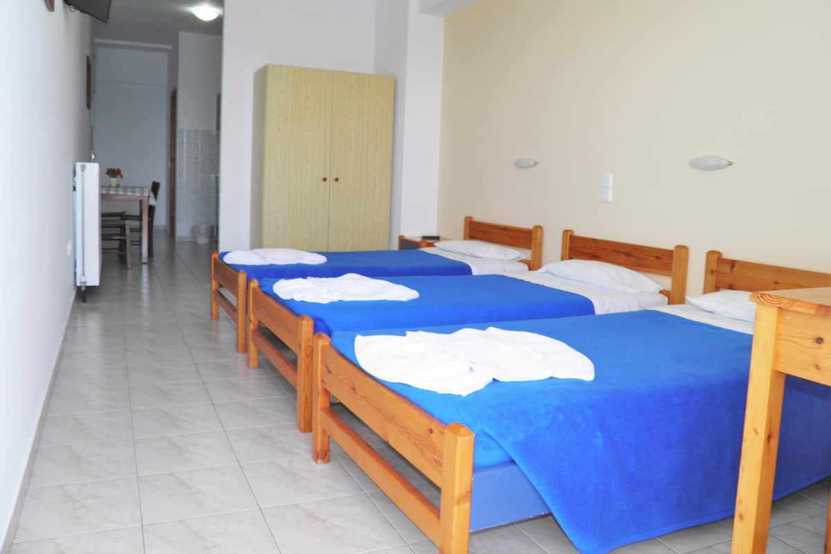 A hotel room with two single beds, a wooden wardrobe, a small table, and a television on the wall.