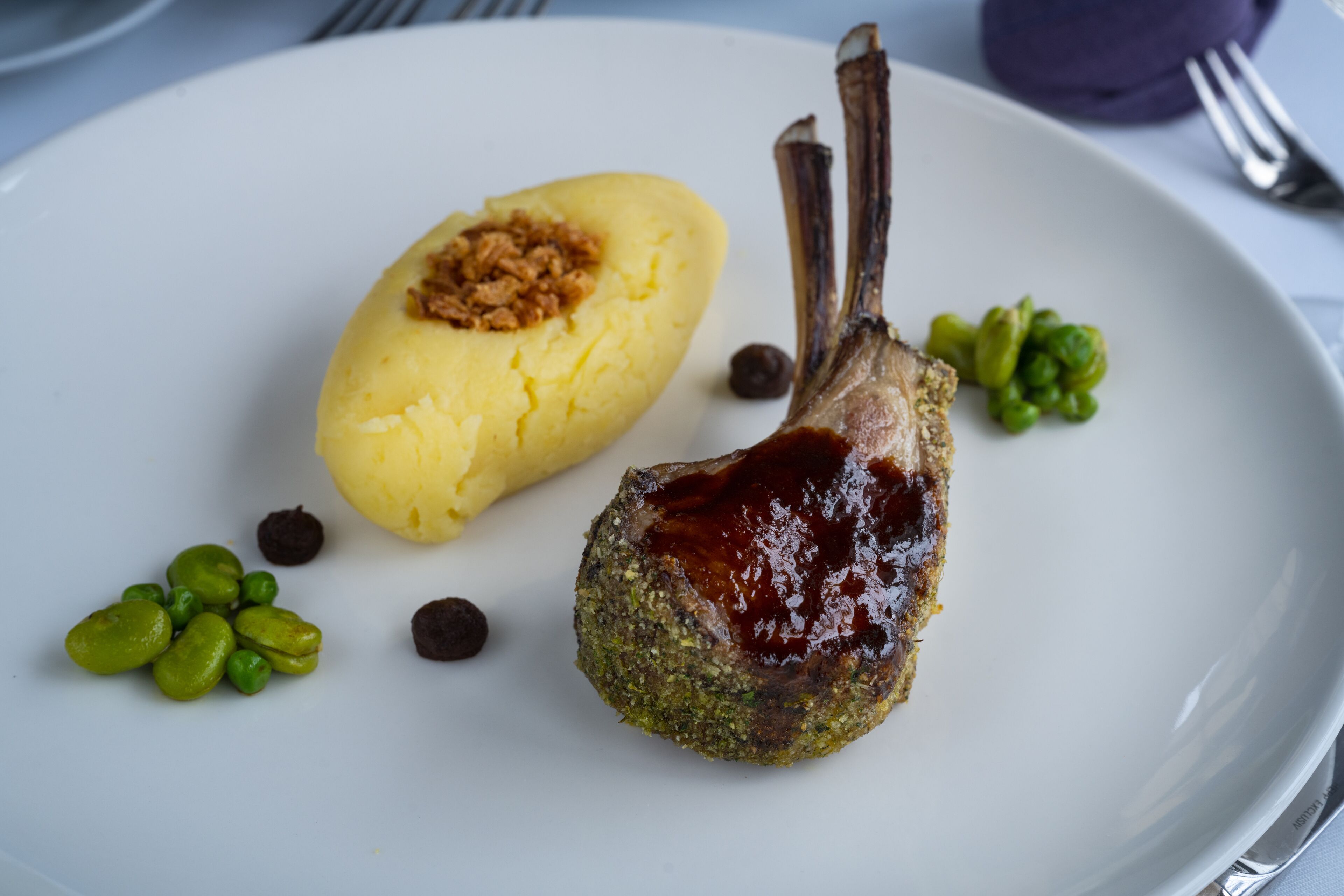 A plate with a lamb chop, mashed potatoes, and green peas.