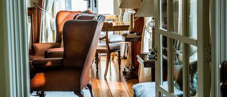 A cozy room with a wooden floor, a leather armchair, a small table with a lamp, and a view through a glass door.