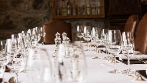 Une longue table à manger, dressée avec de nombreux verres à vin et couverts en argent, sur laquelle se dressent un mur de pierre et des meubles en bois en arrière-plan.