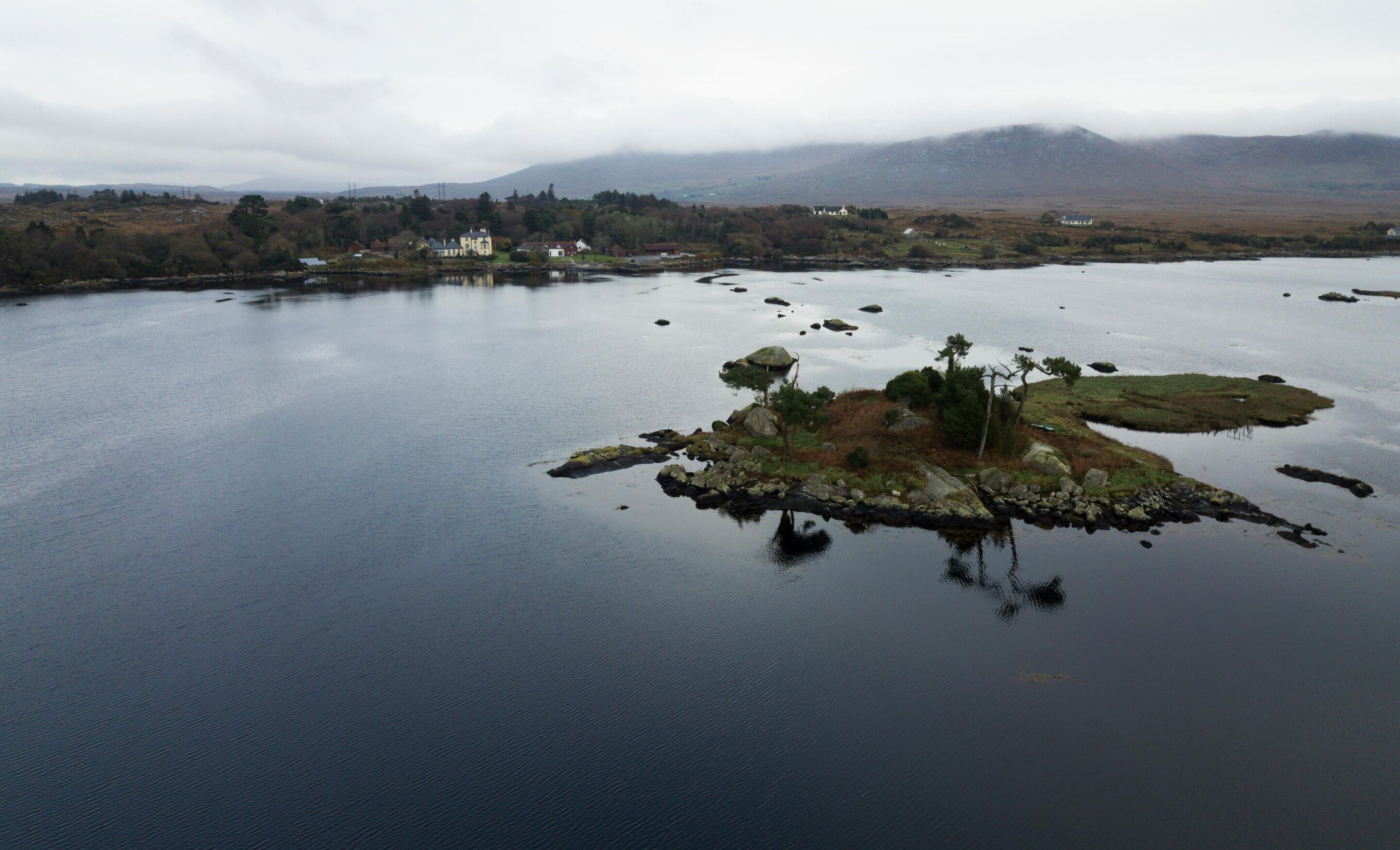 A calm lake with a small island featuring a few buildings and trees.